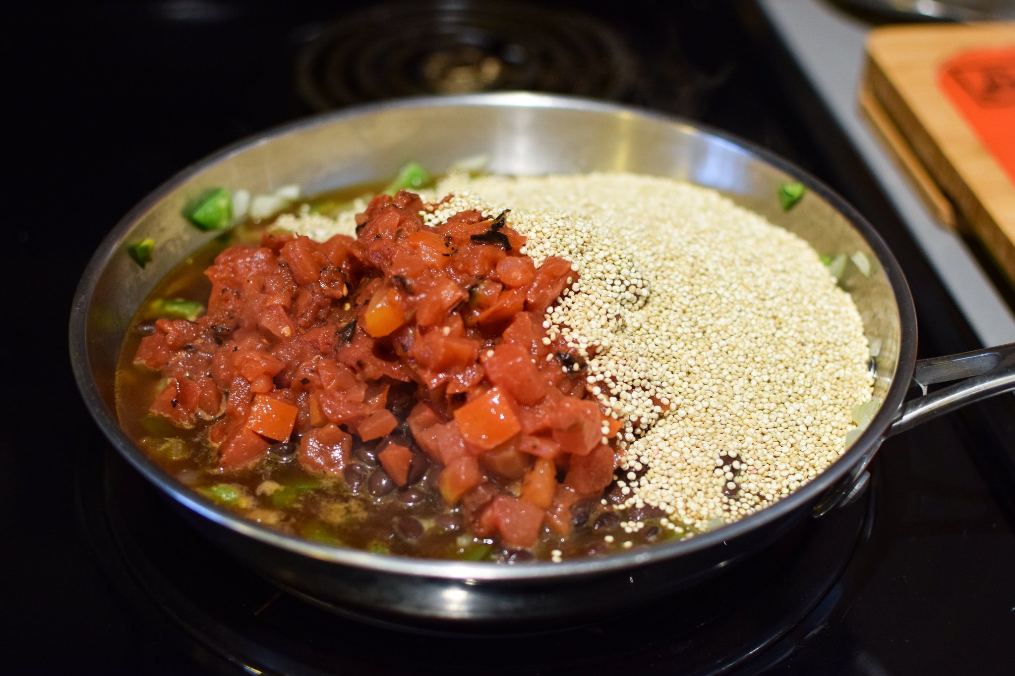 Quinoa and a can of fire roasted tomatoes in a skillet with sauteed onions and jalapeno for mexican quinoa chicken salad lunch bowls.