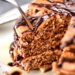 A fork piercing a big stack of Double Chocolate Peppermint Protein Pancakes drizzled with chocolate syrup.