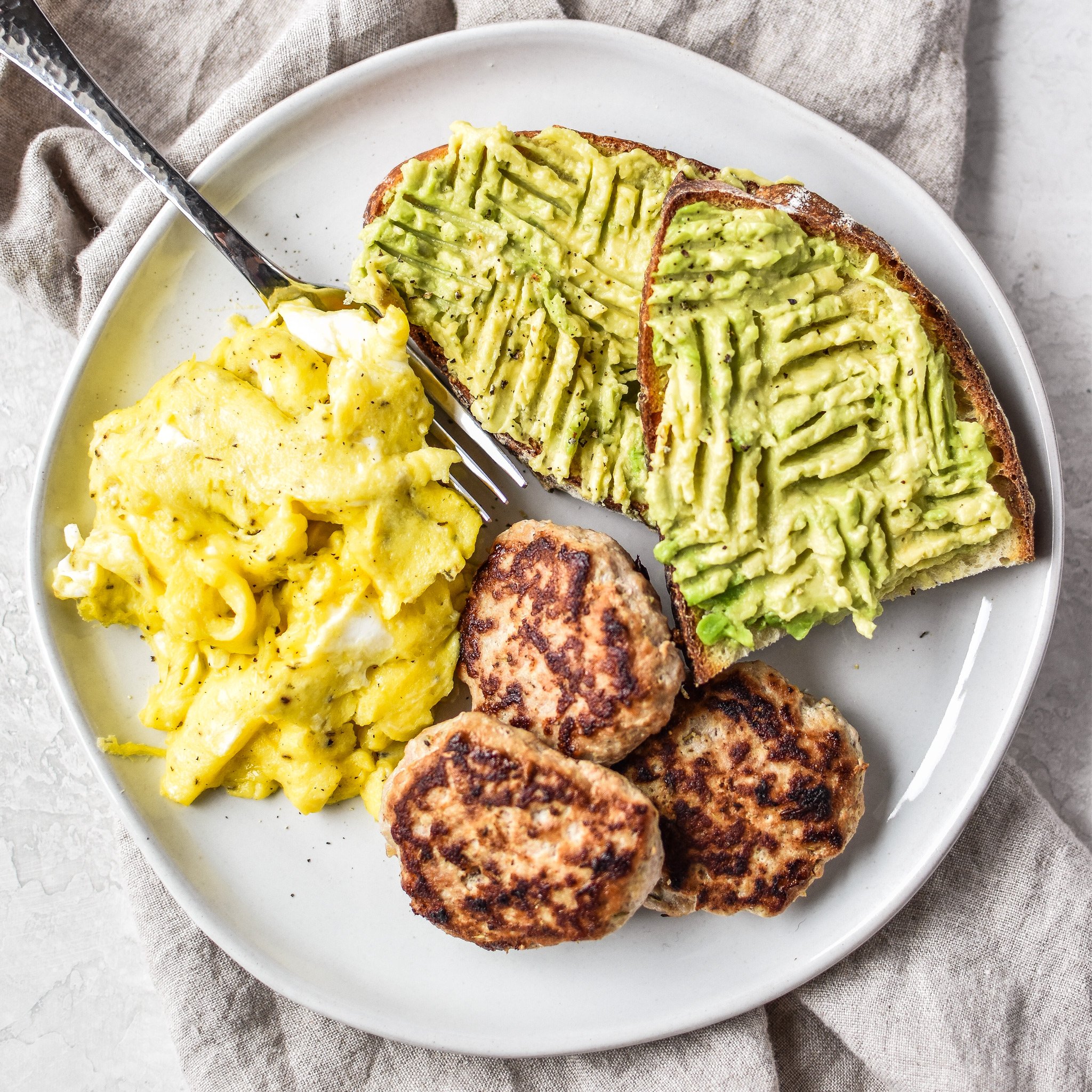 Plate of ground turkey breakfast sausage patties, scrambled eggs and avocado toast.