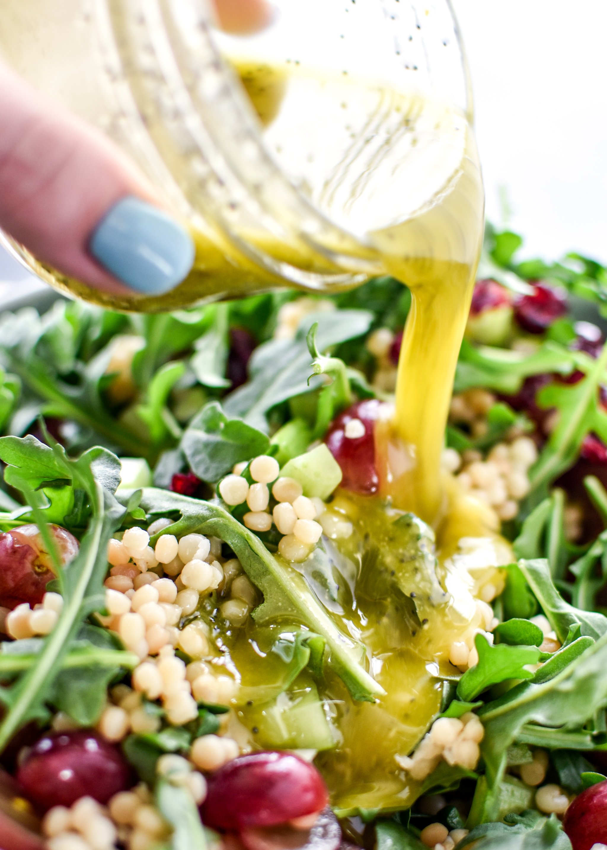 Pouring lemon poppyseed dressing on to the Make Ahead Lemon Poppyseed Couscous Arugula Salad.