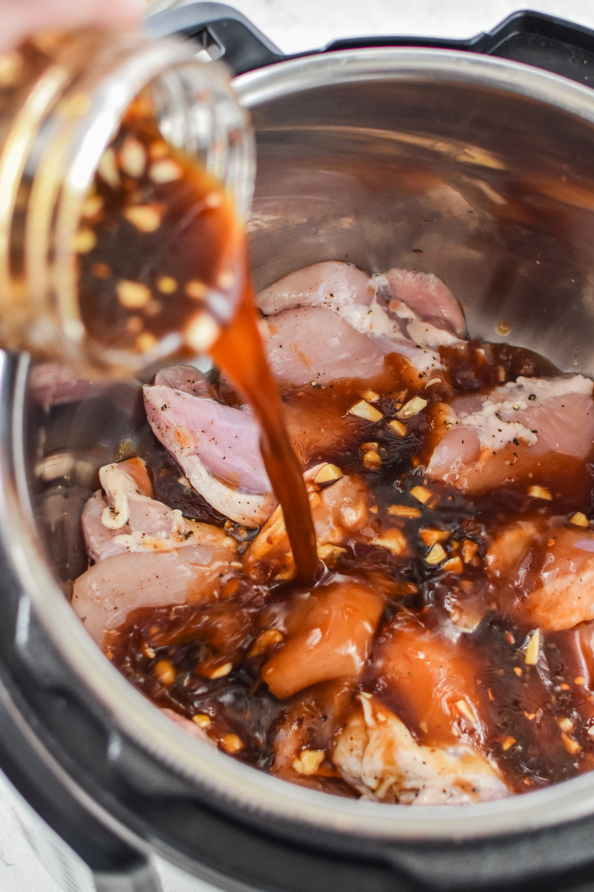 Pouring sauce into the Instant pot for the Instant pot honey garlic chicken meal prep bowls.