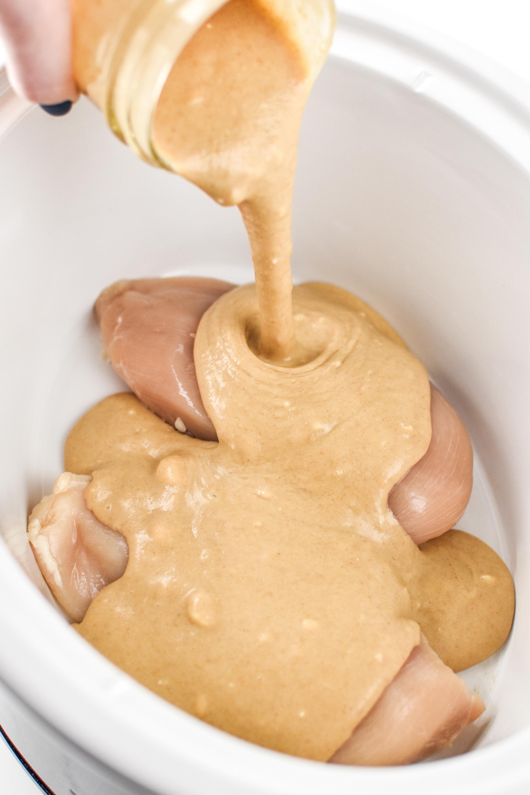 Adding sauce to chicken in the slow cooker for the slow cooker peanut chicken noodles meal prep