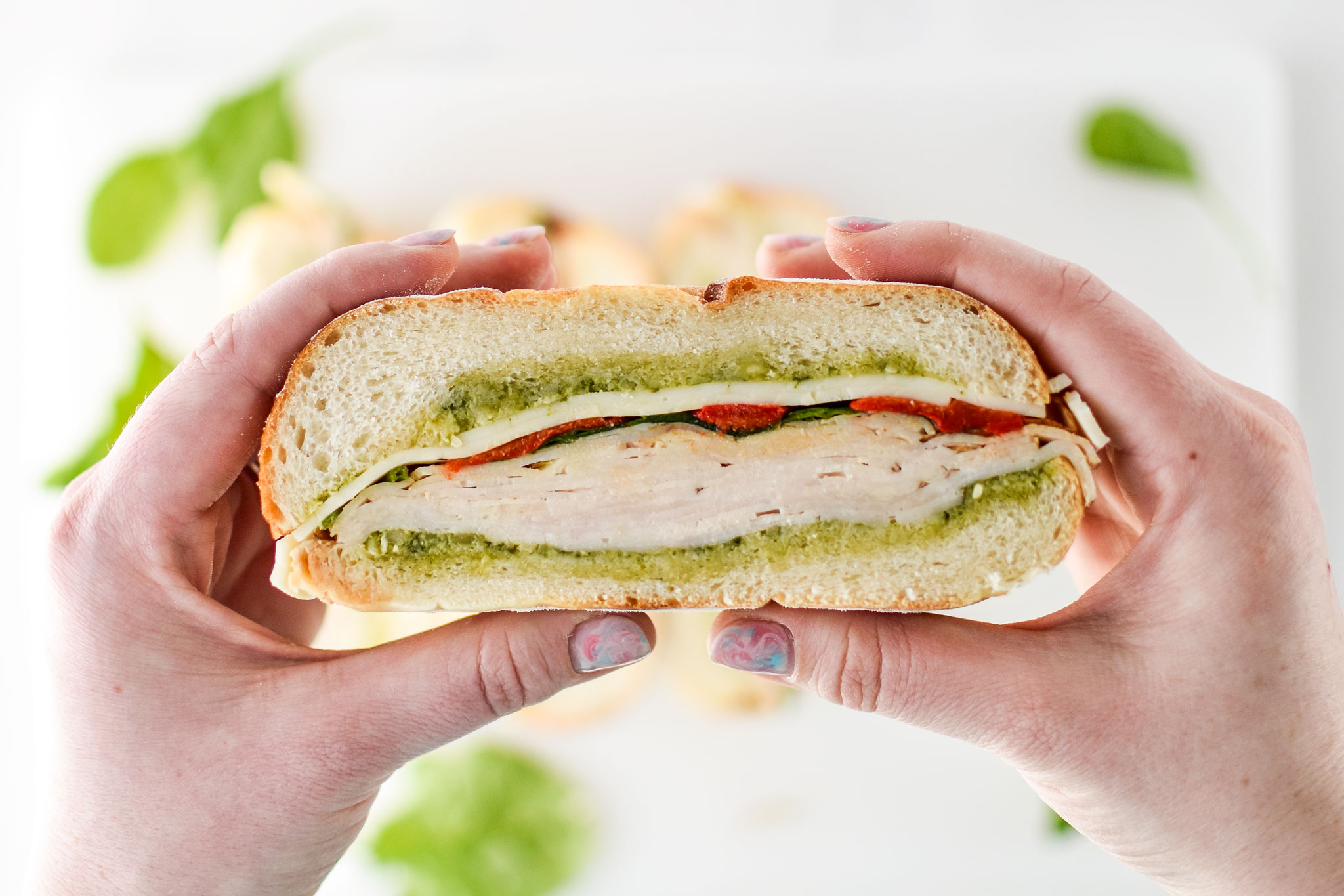 holding a pesto chicken overnight pressed sandwich in hand