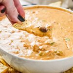 dipping a chip into the chili cheese dip.