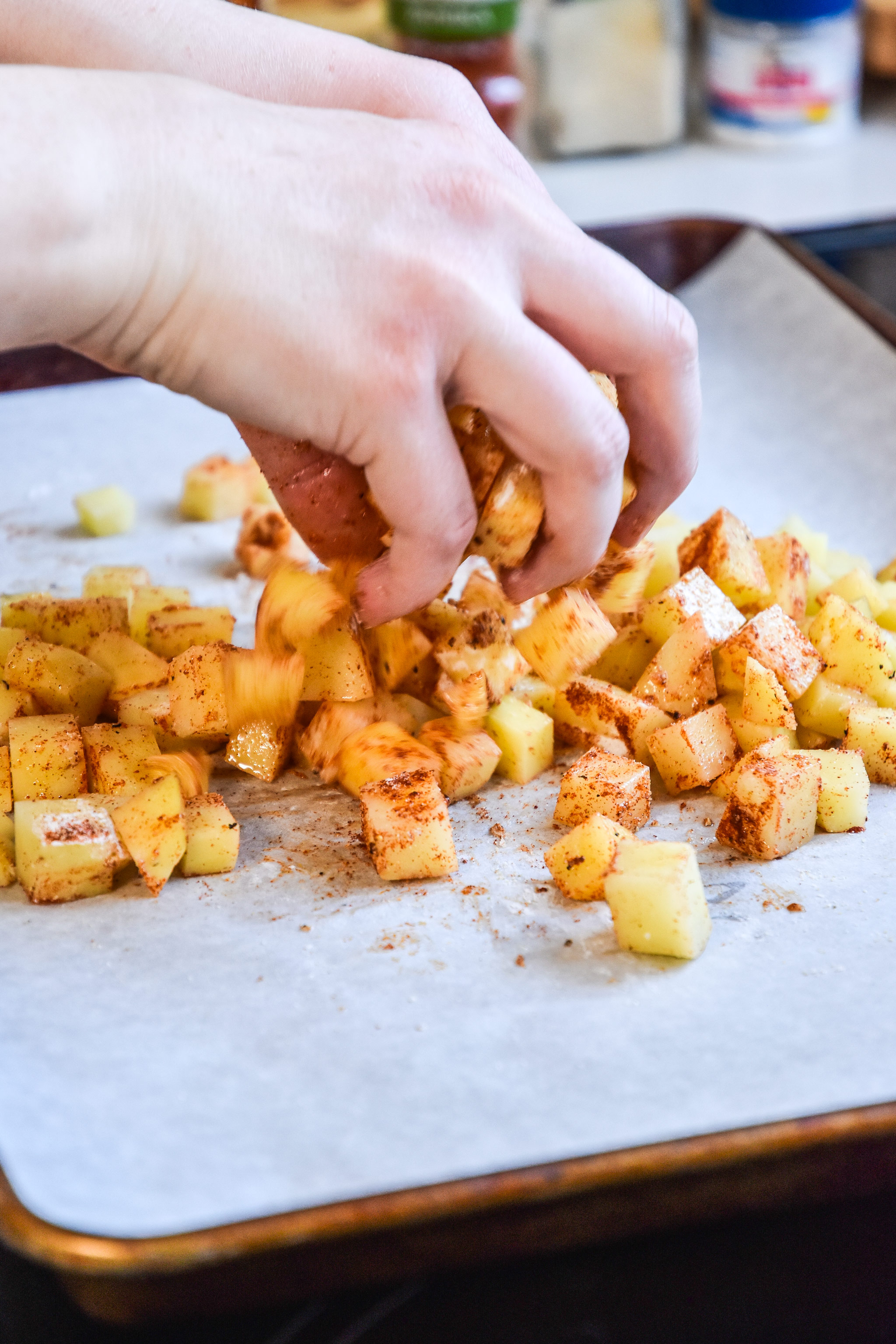 mixing oven potatoes and seasoning on a sheet pan