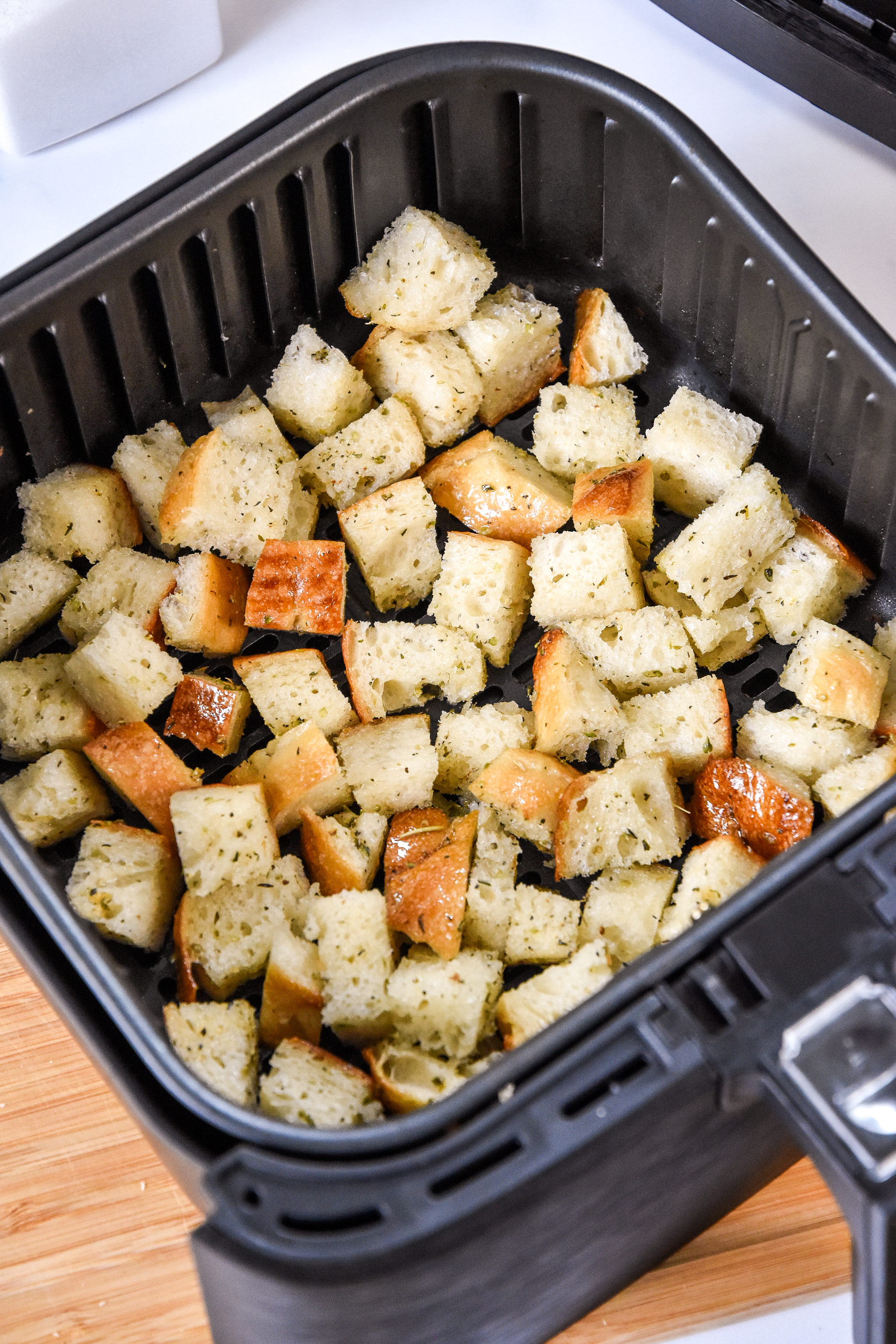 bread cubes in an air fryer basket before cooking.