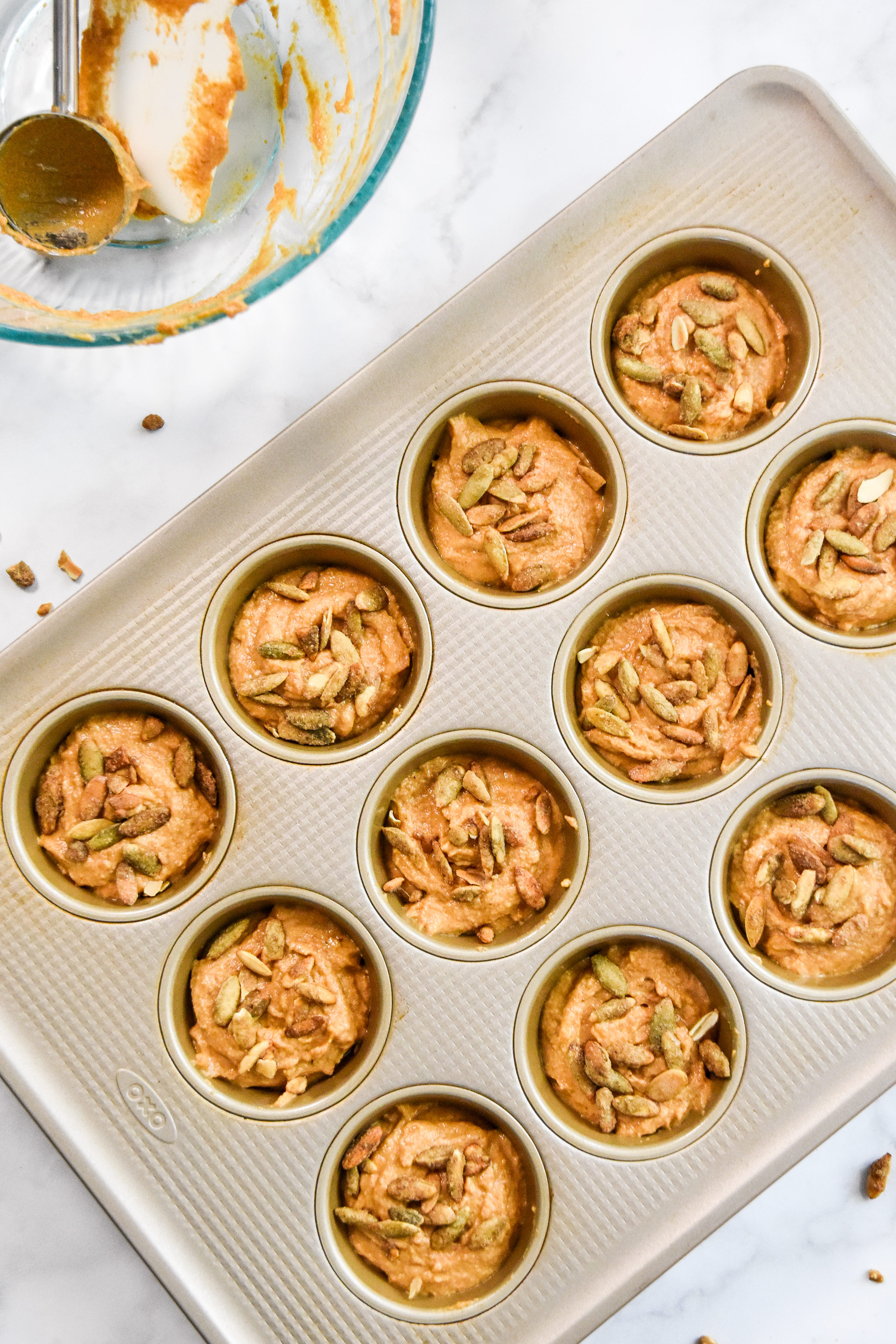 top down view of muffin batter in the baking tin with pumpkin seeds sprinkled on top.