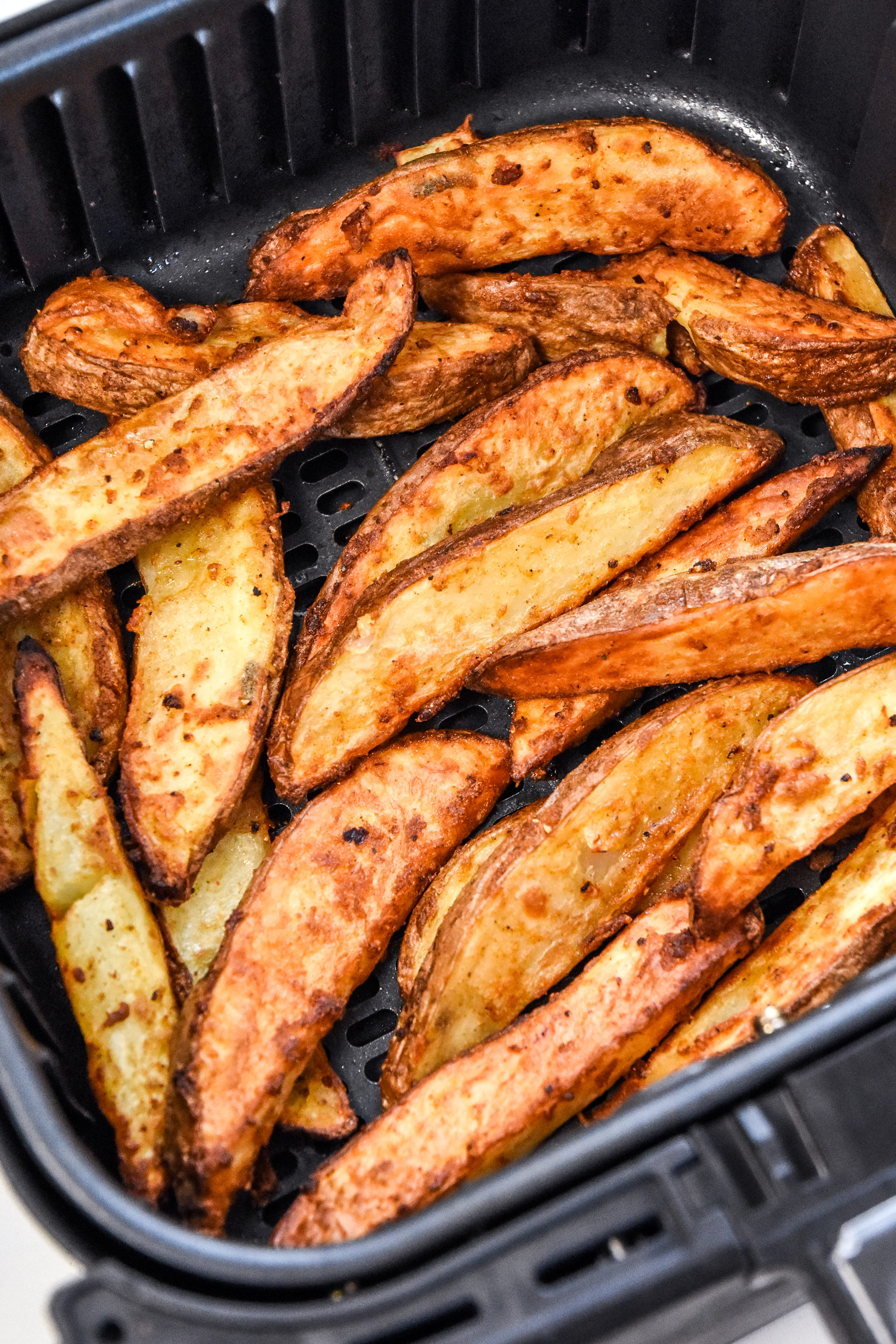 close up of cooked jojo potato wedges in an air fryer basket.