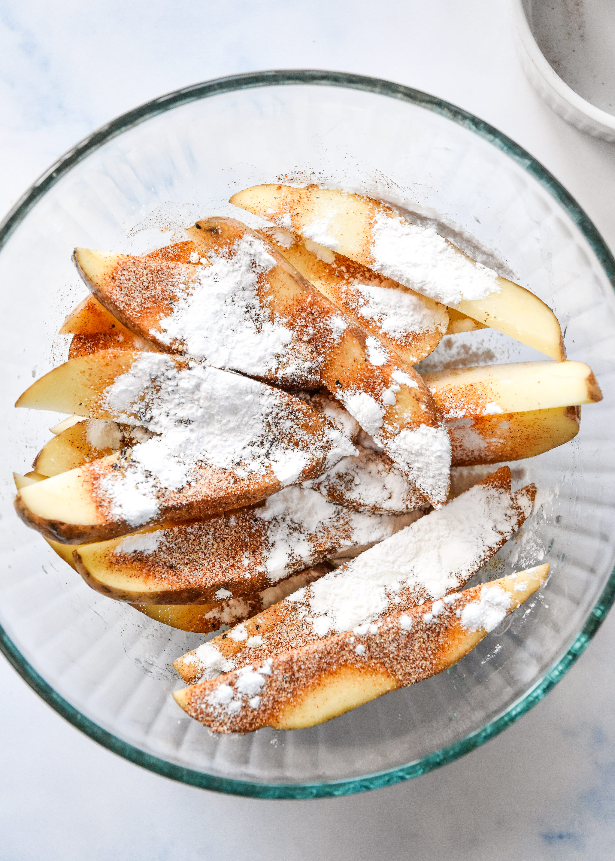 potato wedges in a bowl with oil and spices on top.