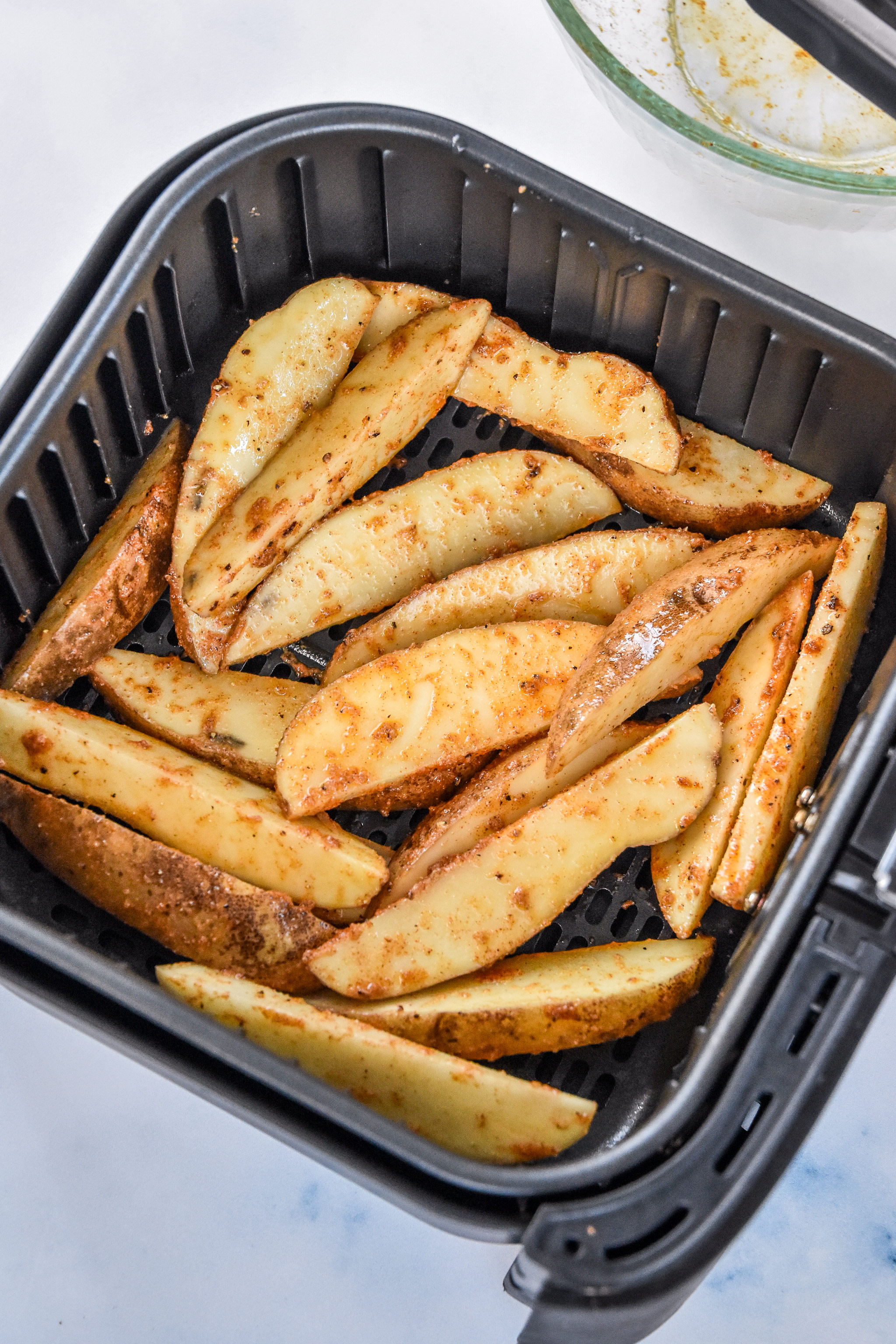 raw jojo potato wedges in an air fryer basket.