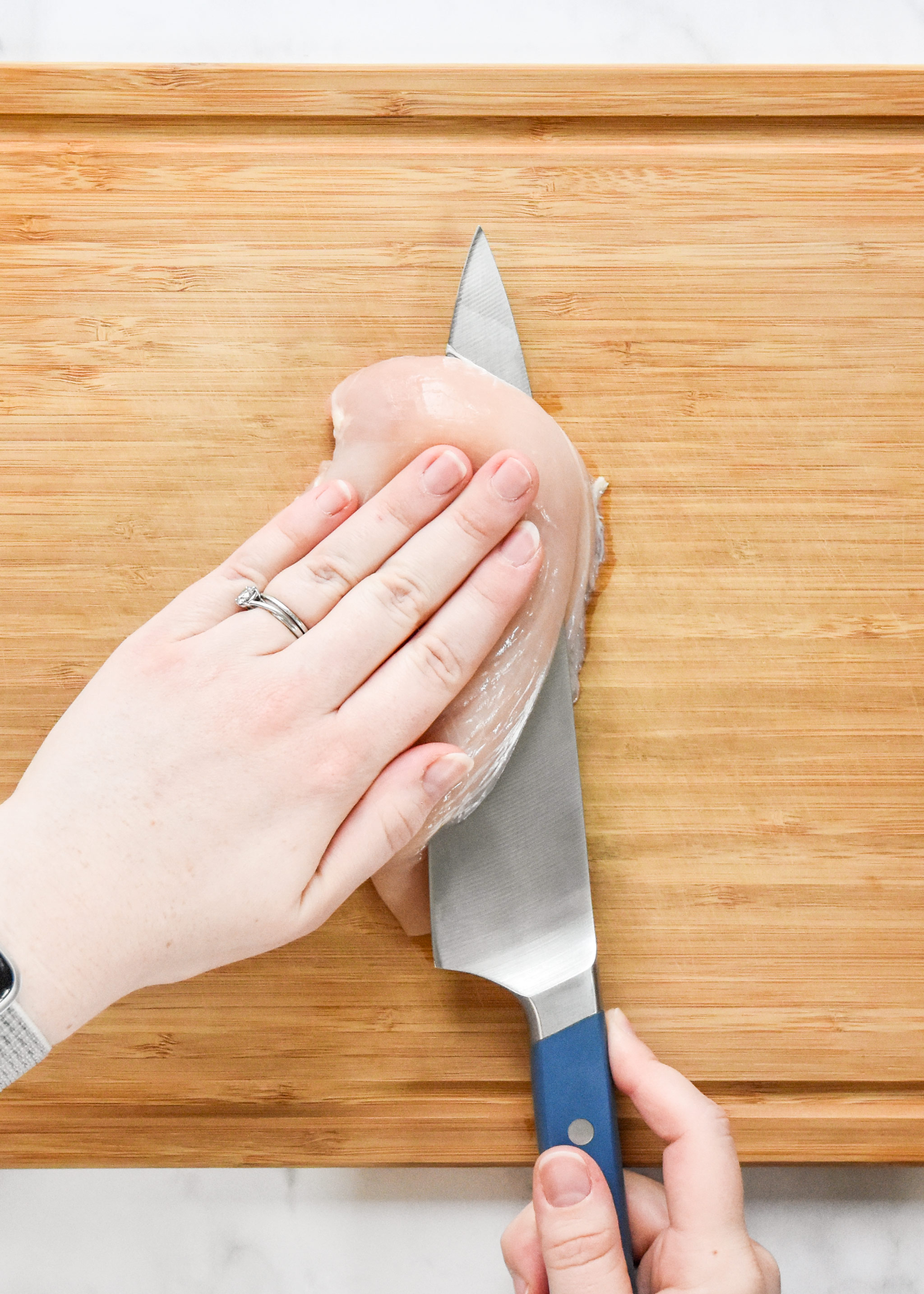 cutting chicken breast in half with a chefs knife.