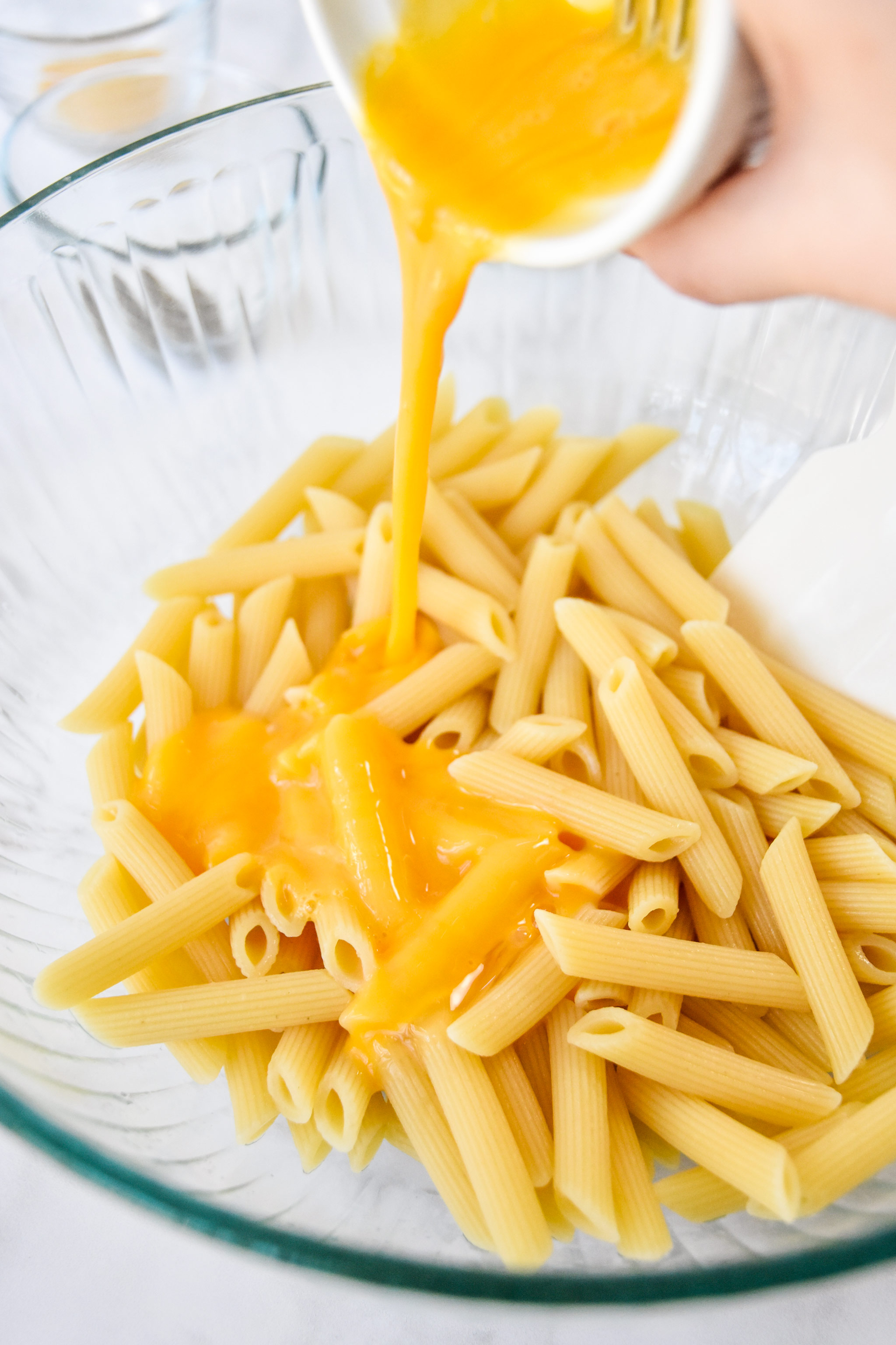 pouring egg into the bowl of cooked pasta.