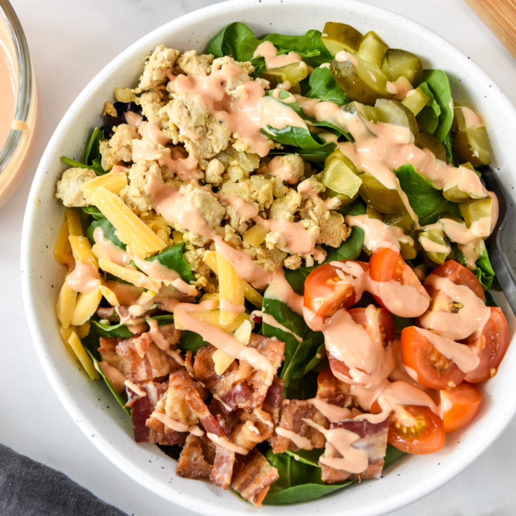 ground turkey burger salad with bacon cheese pickles, serve in a white bowl with special sauce dressing.