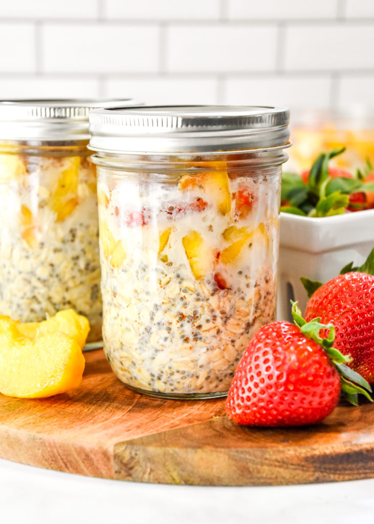 mason jar full of strawberry peach overnight oats on a cutting board.