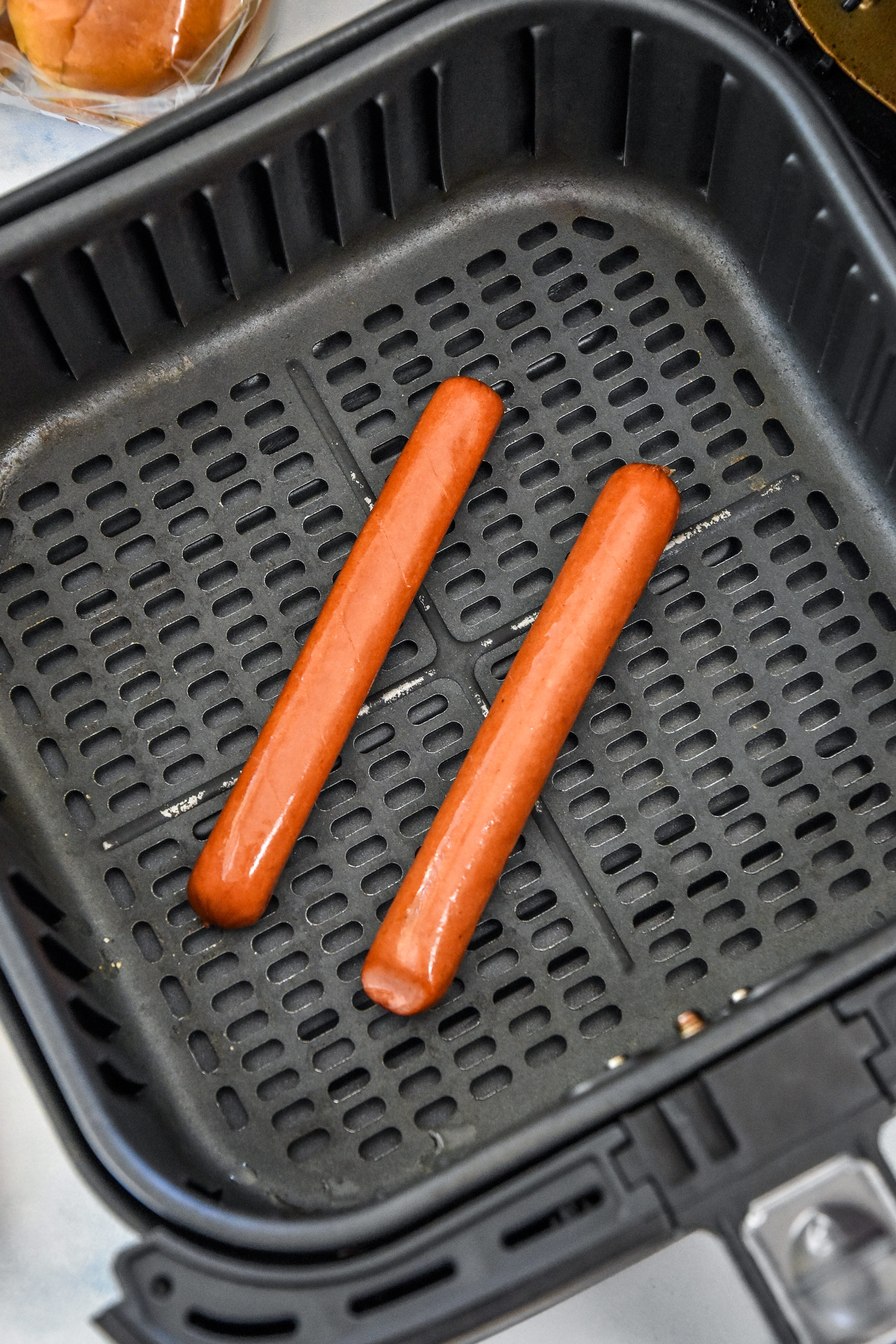 hot dogs in the air fryer basket about to be cooked.