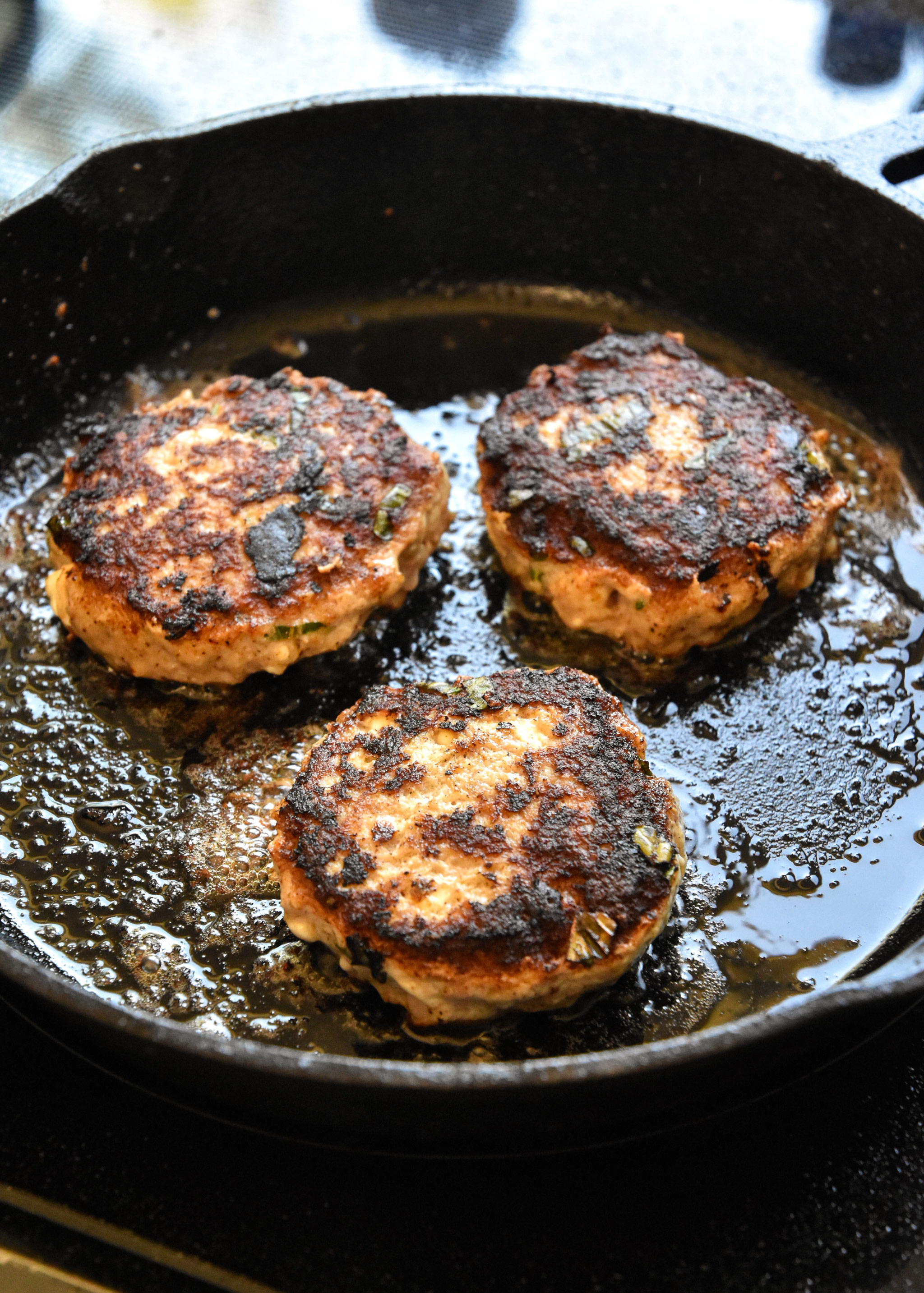 feta basil turkey burgers cooking in a cast iron skillet.