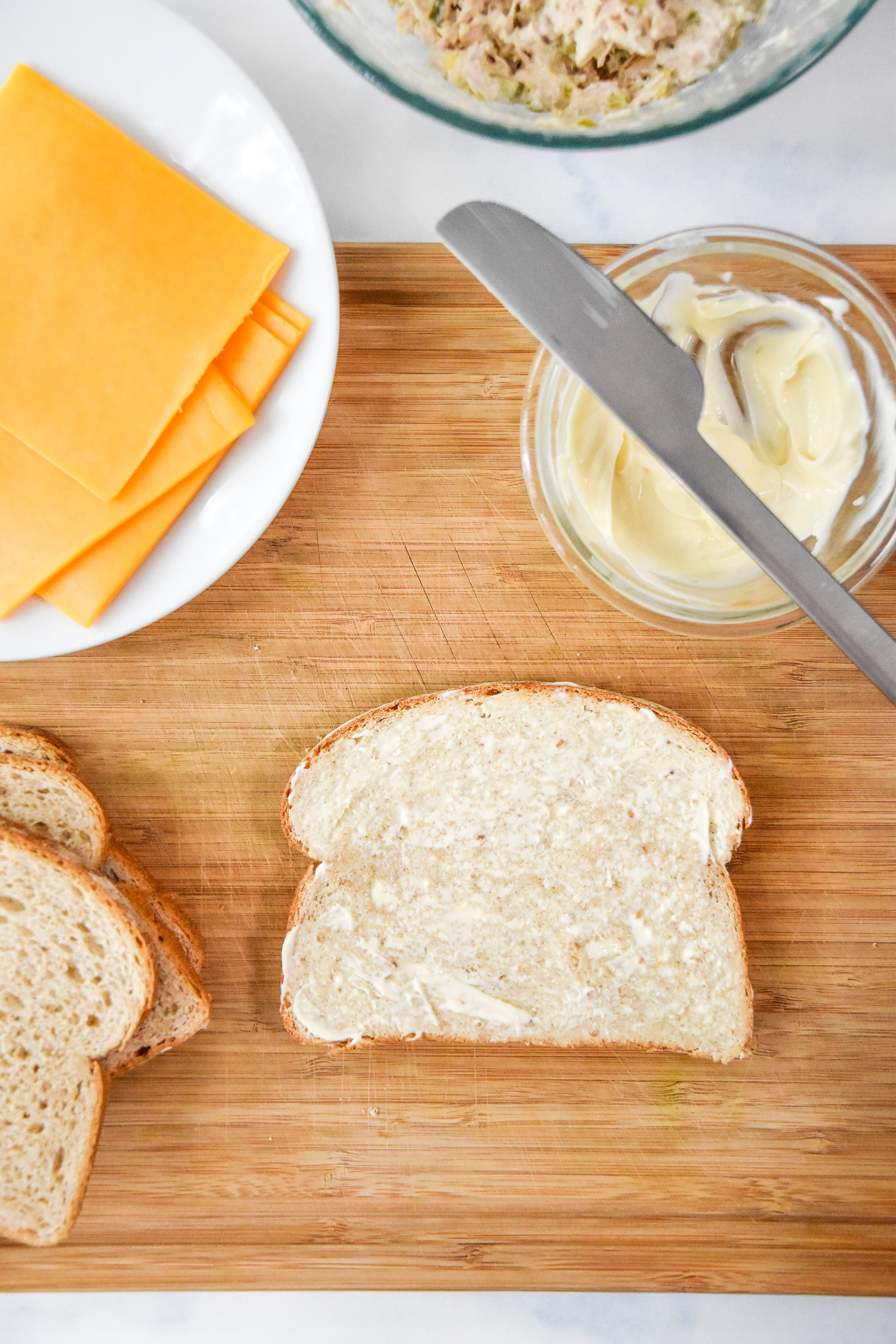 a piece of bread covered with mayo on one side laying on a cutting board.
