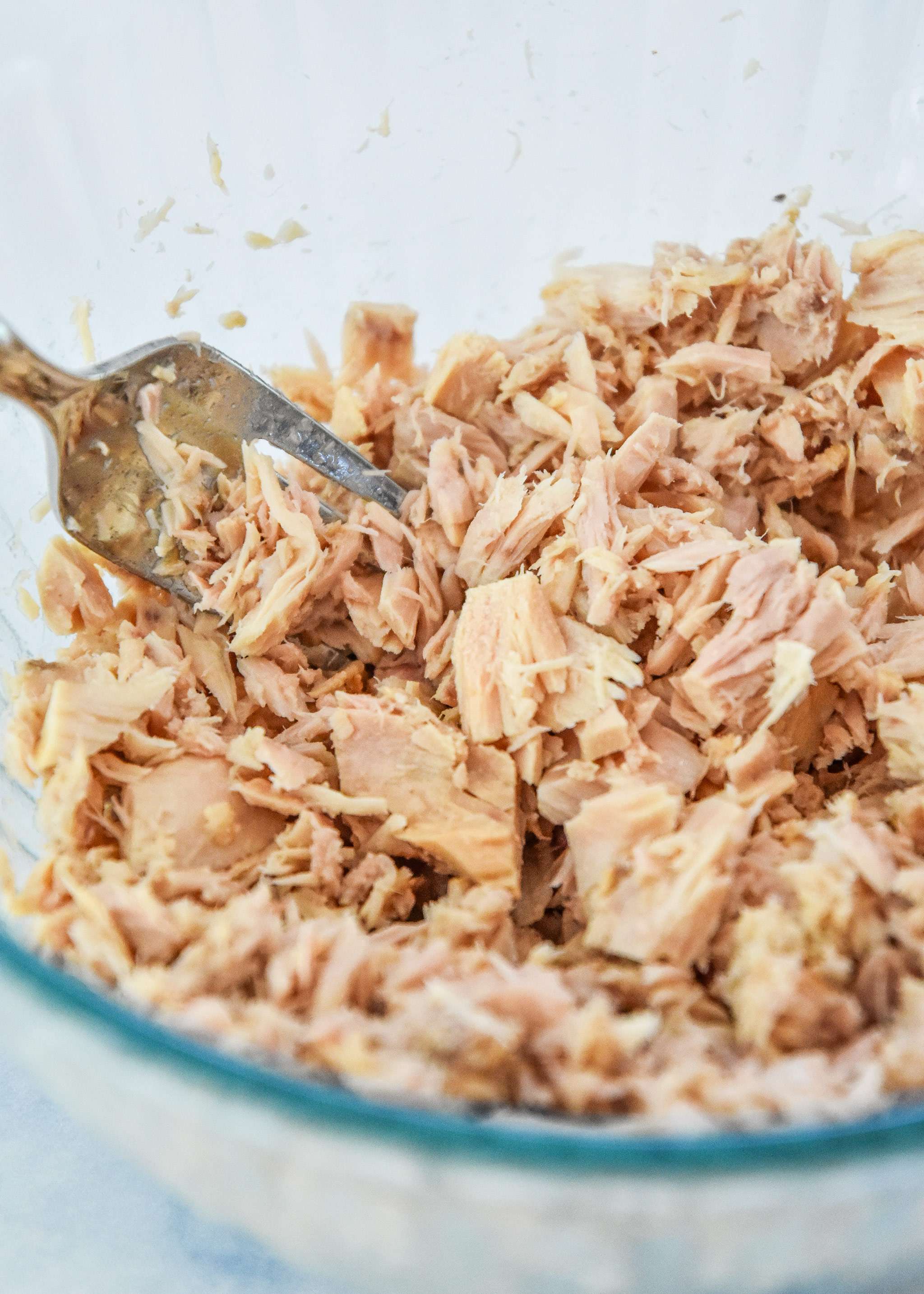 flaking tuna with a fork in a glass bowl.