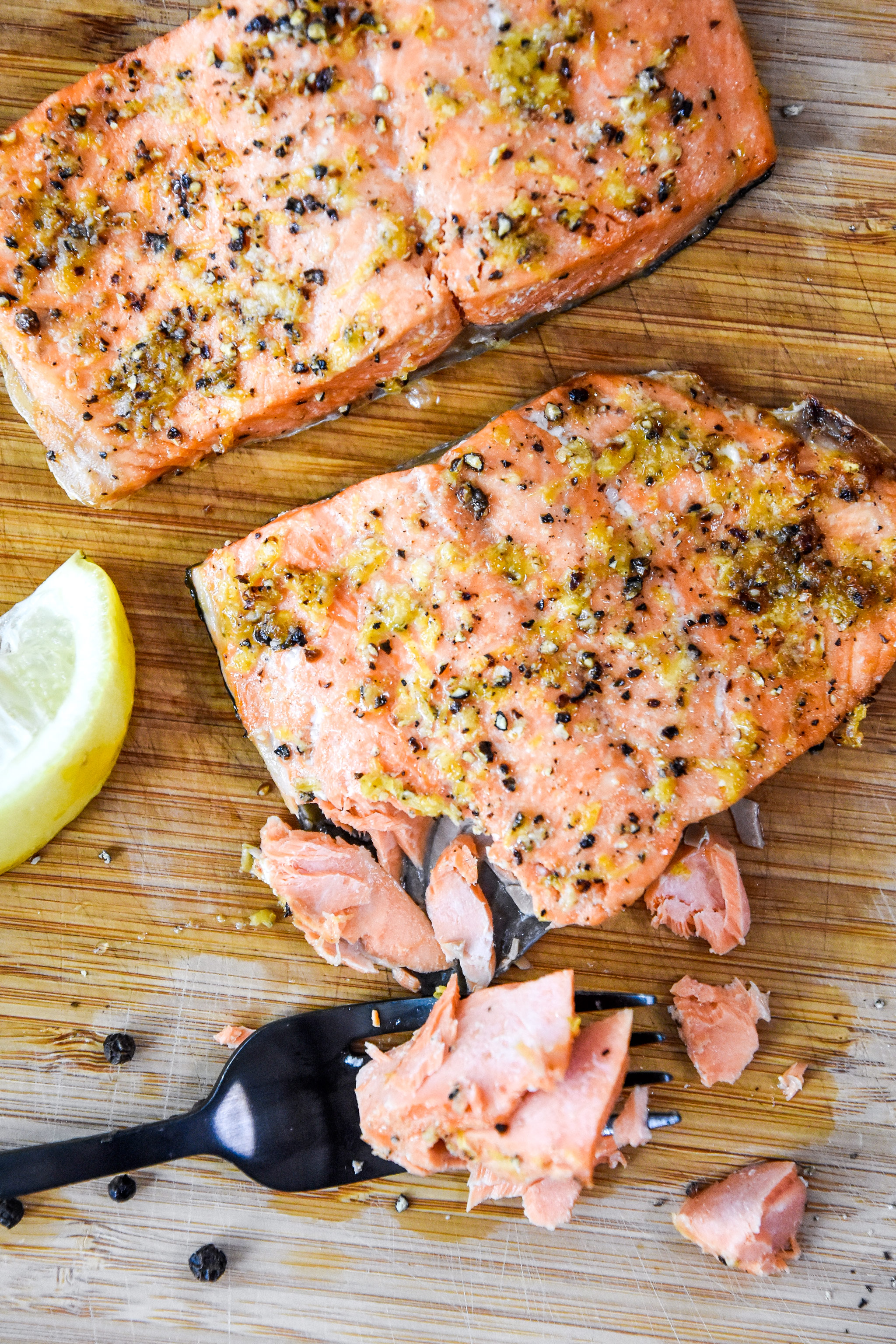 cooked lemon pepper salmon on a cutting board flaked with a fork.