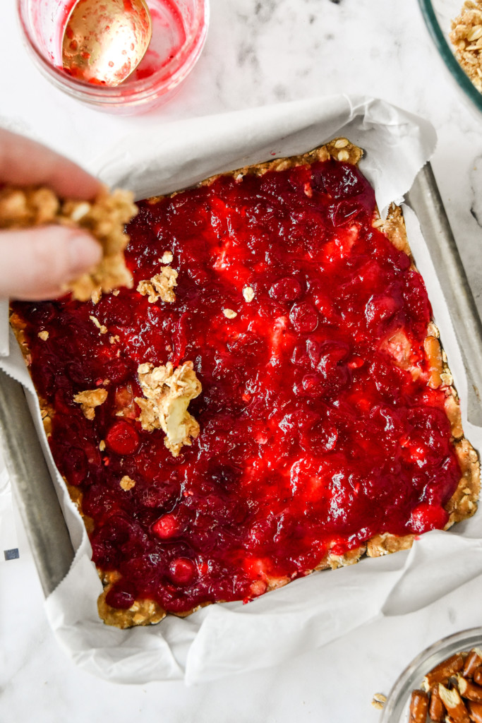 cranberry sauce covering the base layer of crumble mixture in an 8x8 pan for the cranberry pretzel oat crumble bars.