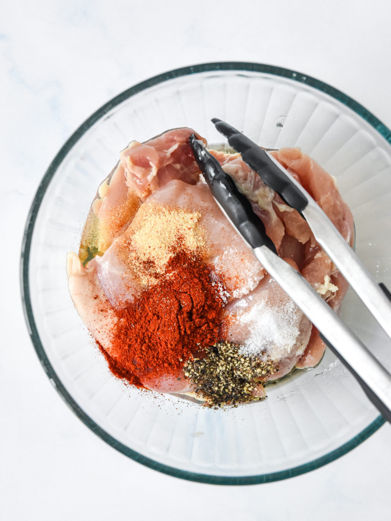 spices and oil with the chicken in a bowl about to be mixed up.