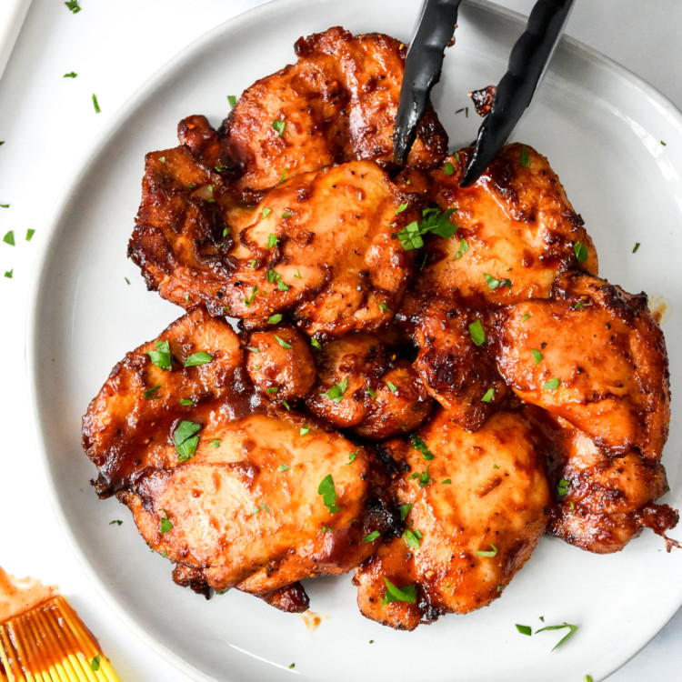 air fryer boneless bbq chicken thighs on a plate with tongs.