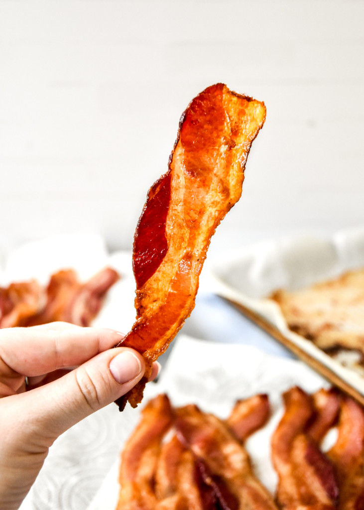 holding a cooked piece of bacon in hand.