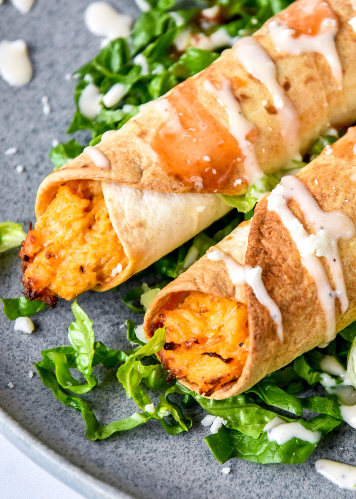 plated air fryer buffalo chicken flautas or taquitos with shredded lettuce and buffalo sauce.