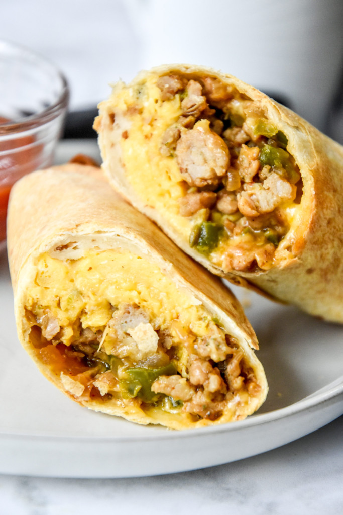 cut in half burrito in a plate with a cup of salsa.