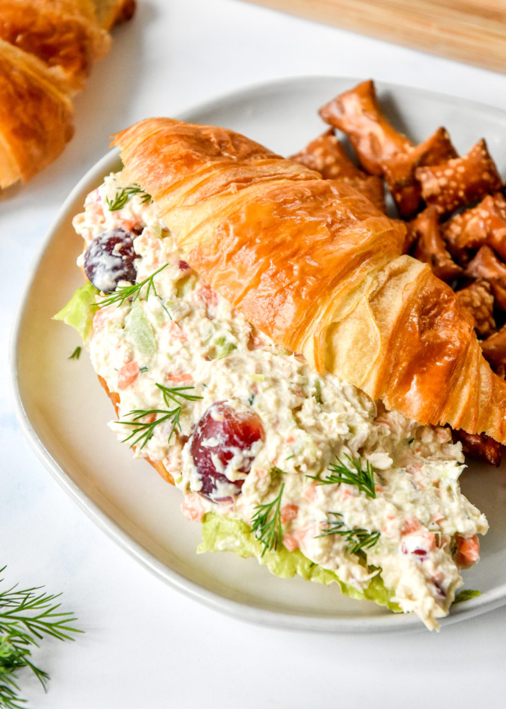 chicken salad croissant sandwich on a plate with pretzels.