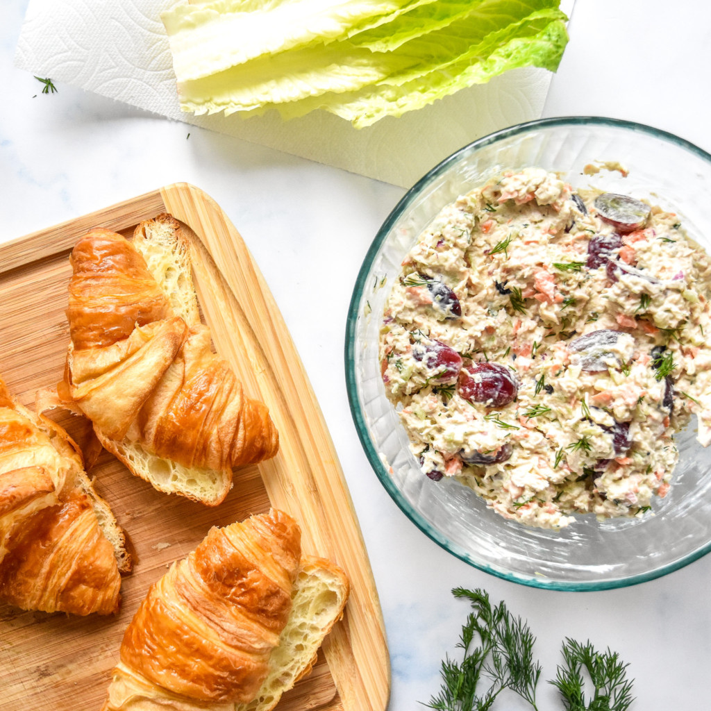 bowl of chicken salad next to a cutting board with croissants and lettuce.