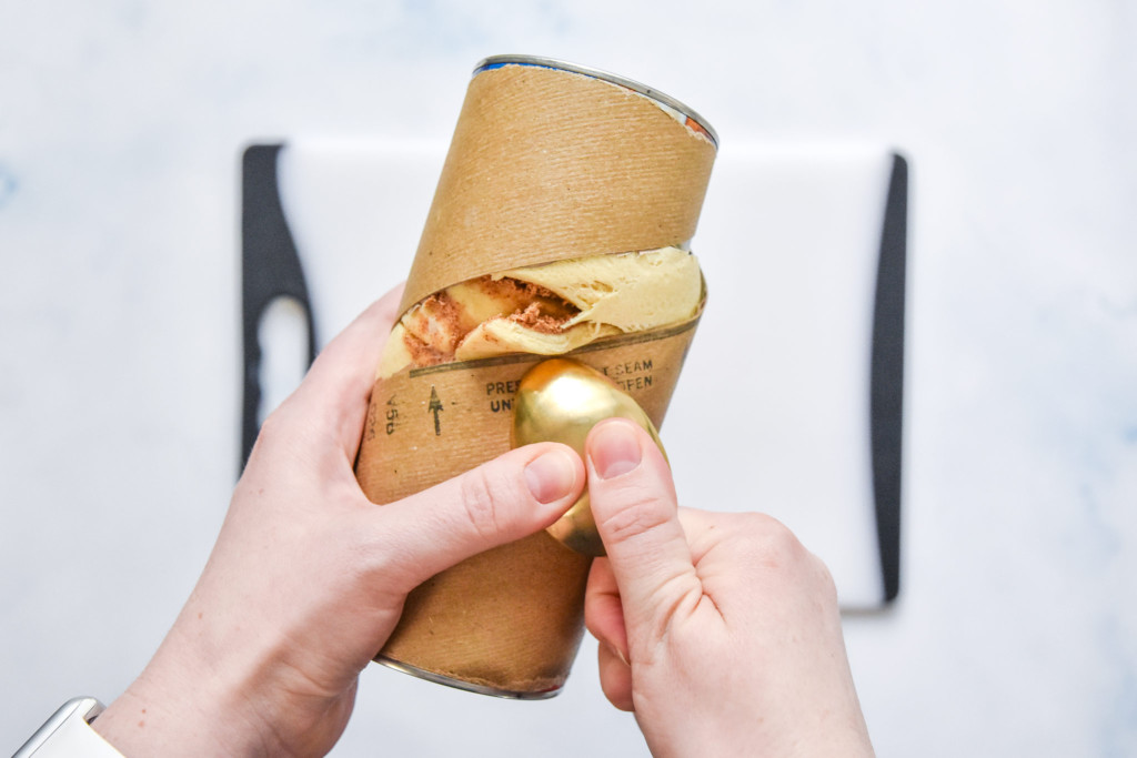 using a spoon to open a can of cinnamon rolls.