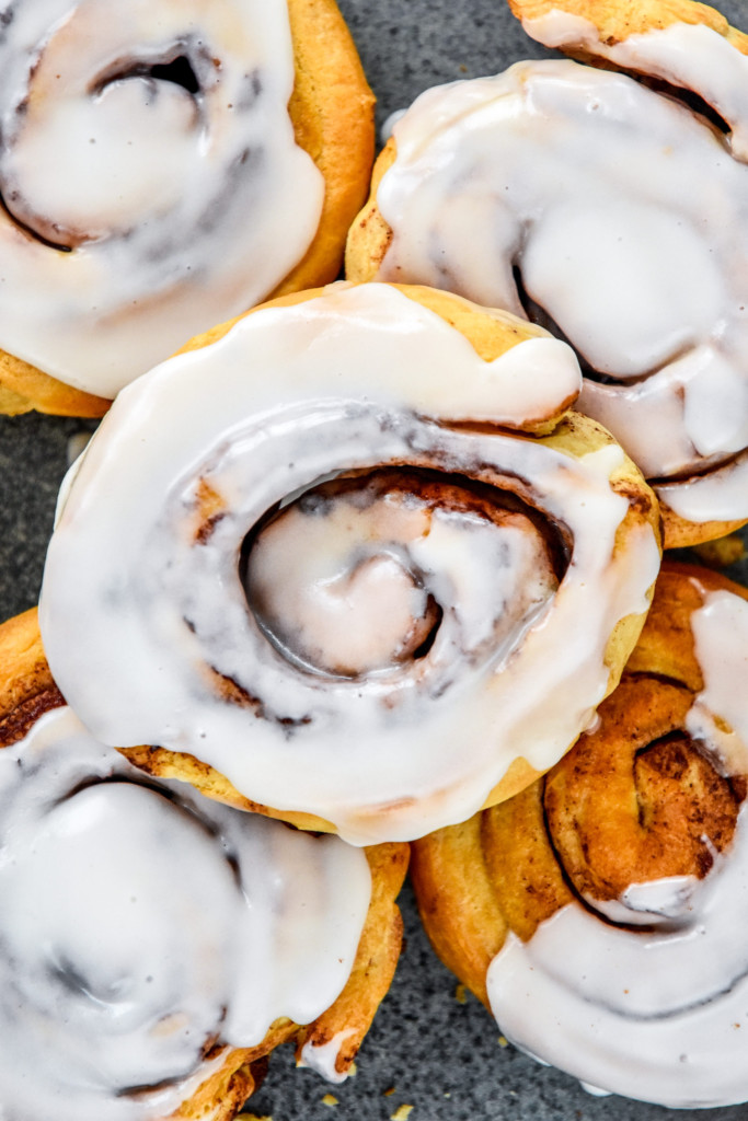 close up air fryer canned cinnamon roll with icing on a plate.