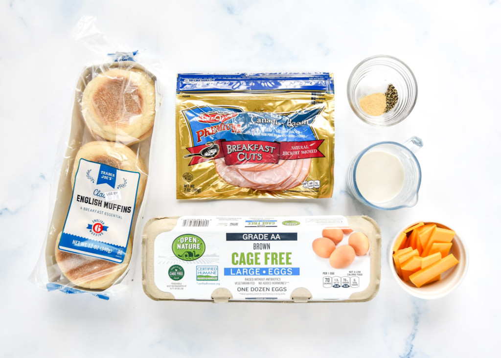 breakfast sandwich ingredients on a table including english muffins and eggs in a carton.