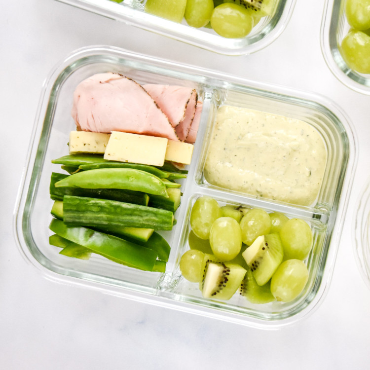 close up of green food lunch box meal prep with peppered turkey, havarti cheese, green fruits and veggies.
