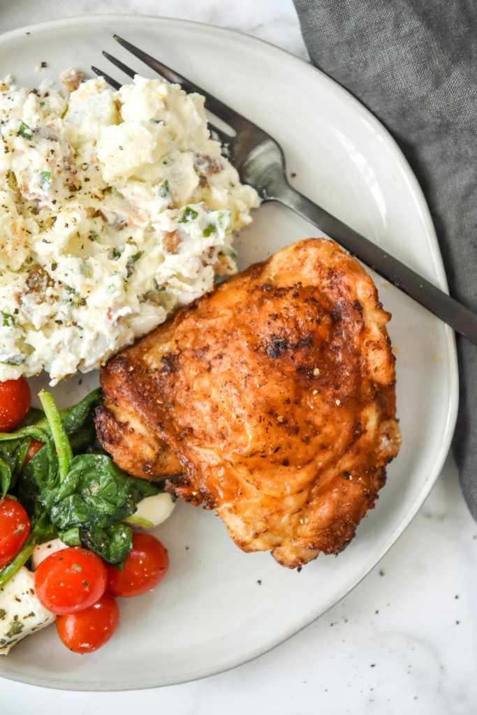 plated crispy chicken thigh with caprese salad and potato salad on a plate.