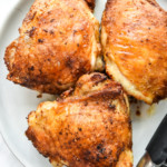 three air fryer bone-in crispy chicken thighs on a plate.