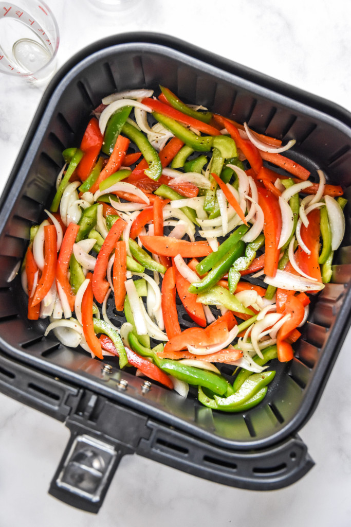 peppers and onions in the air fryer basket to make air fryer sausage dogs with peppers and onions.