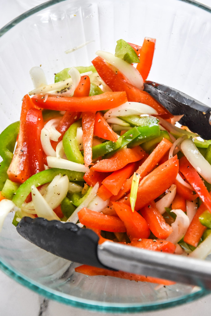 mixing up peppers and onions in a bowl with tongs.