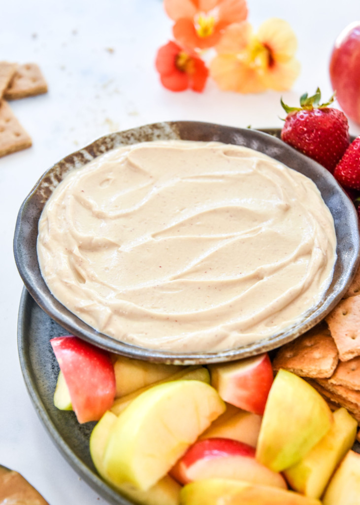 peanut butter greek yogurt fruit dip on a plate with fruit and graham crackers.