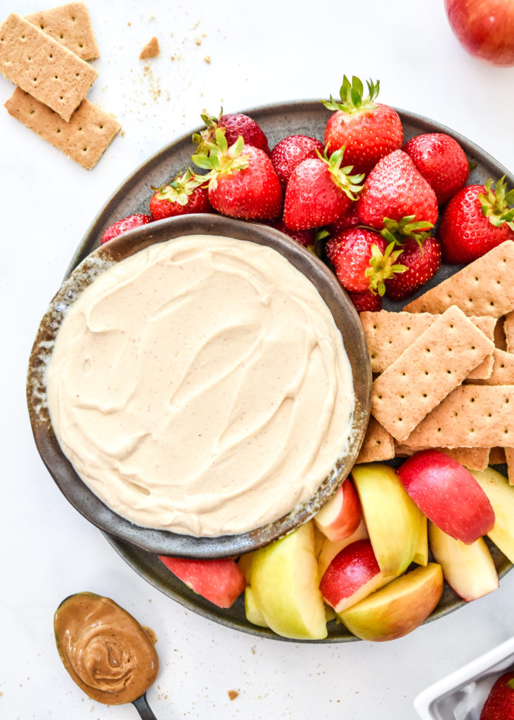 peanut butter greek yogurt fruit dip in a bowl with cut apples and strawberries.