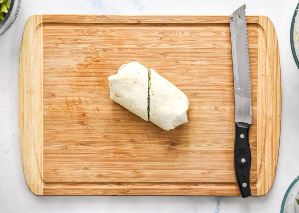 prepared caesar chicken salad lunch wrap cut in half on a cutting board.