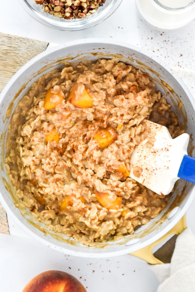 cooked peaches and cream oatmeal in a sauce pan.