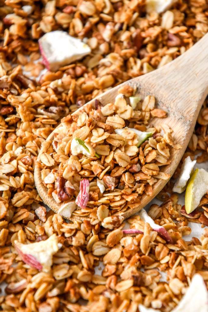 homemade apple pie spiced granola on a sheet pan with wooden spoon.