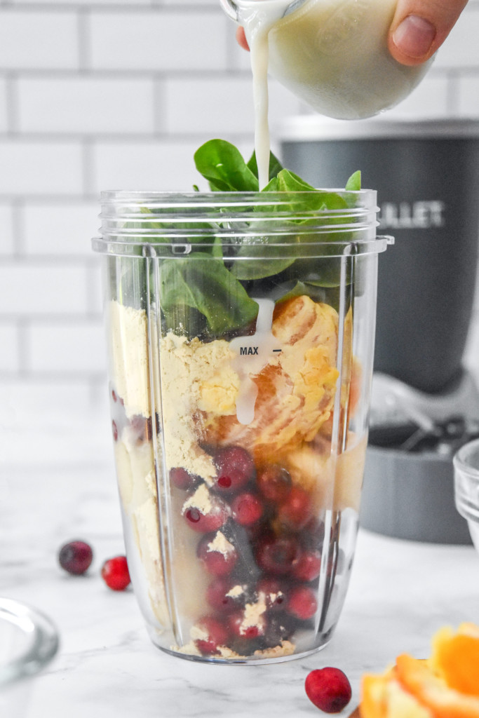 adding all ingredients to the blender to make the orange cranberry cinnamon holiday smoothie.