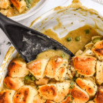 spoonful of chicken pot pie with biscuit crust in a white oval dish.