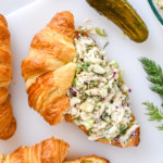 dill pickle chicken salad on a croissant on a cutting board.