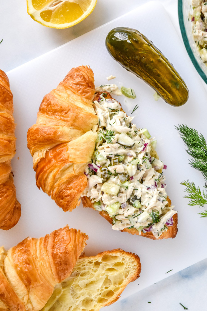 dill pickle chicken salad on a croissant on a cutting board.