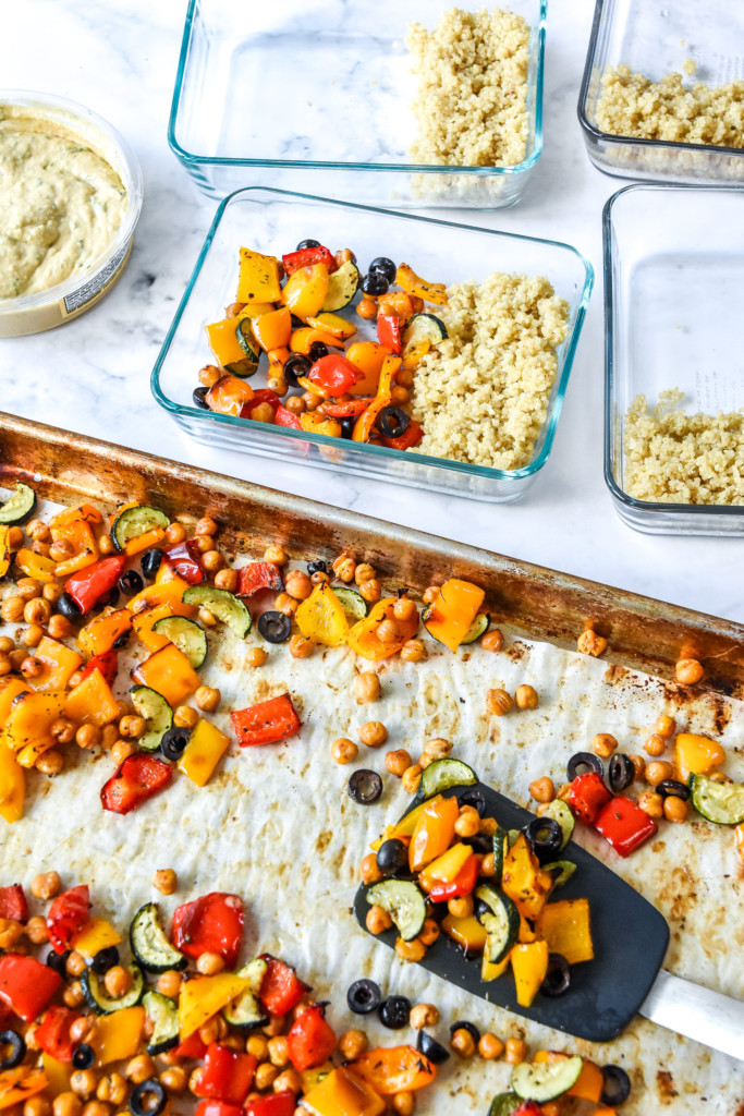 portioning the roasted vegetables into glass meal prep containers for the mediterranean inspired grain bowl meal prep.