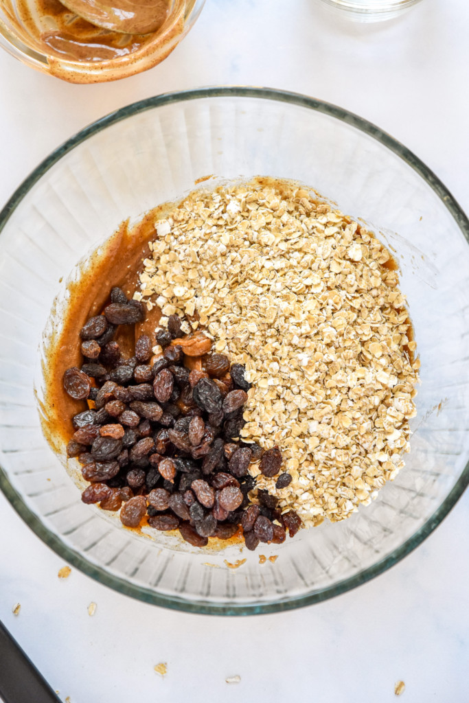 ingredients for the no-bake oatmeal raisin cookie balls being mixed in a glass bowl.